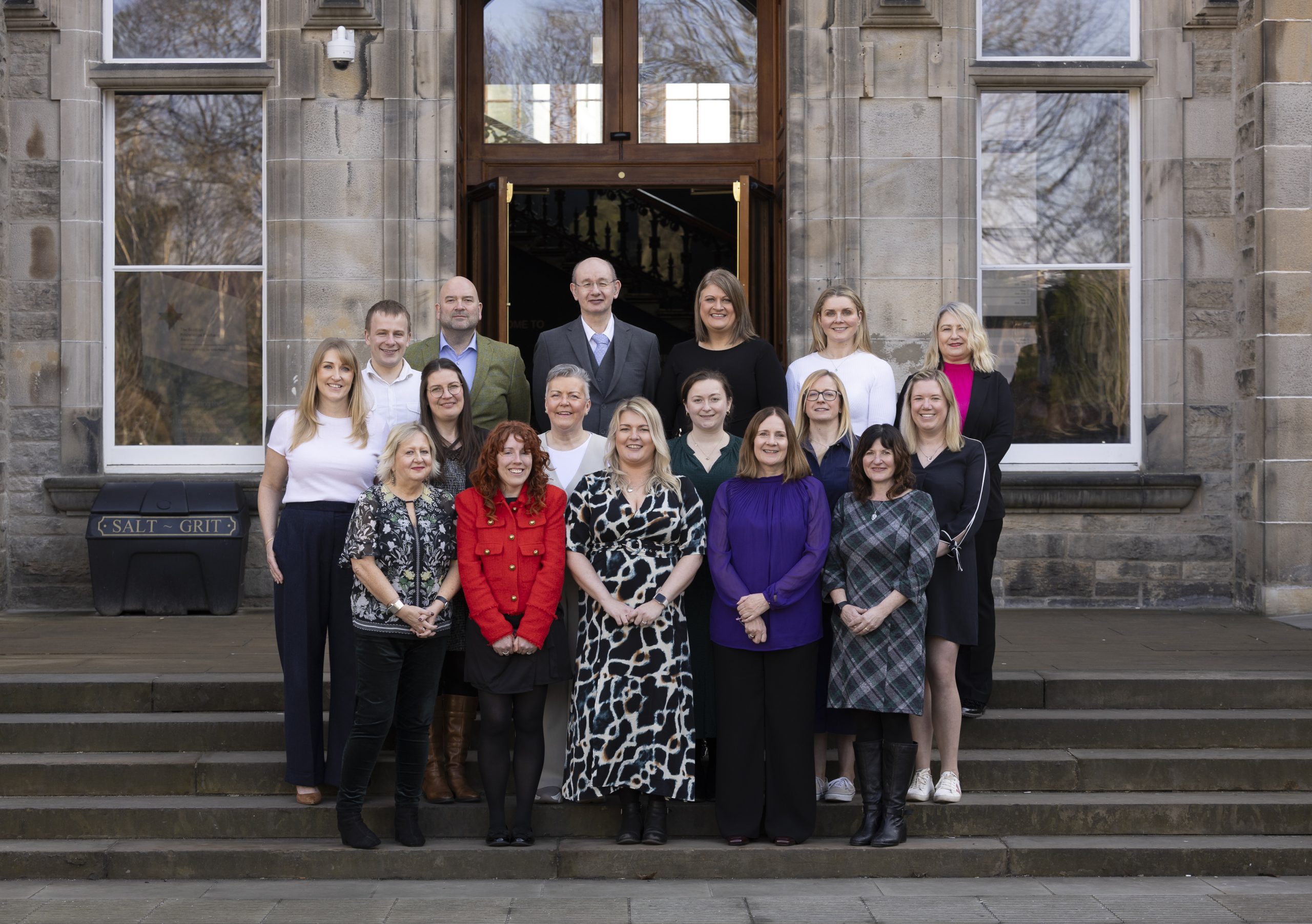 A photograph of the Interface team stood on steps outside of a university building. The team are smiling and looking down the camera.